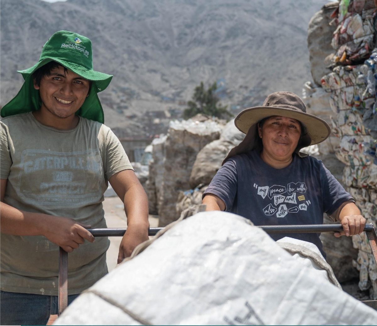 Una mujer recicladora y un joven reciclador sonríen junto a su carreta con sacos de material recuperado
